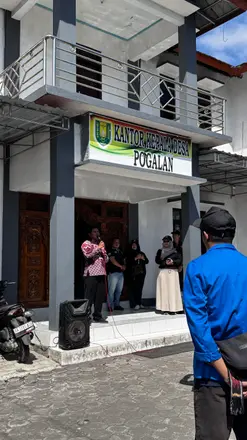 Perangkat desa dan mahasiswa berdiri di depan pintu Kantor Kepala Desa Pogalan saat penyambutan