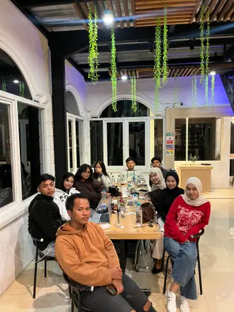 Mahasiswa dan warga berkumpul mengitari meja panjang di dalam rumah pada malam hari