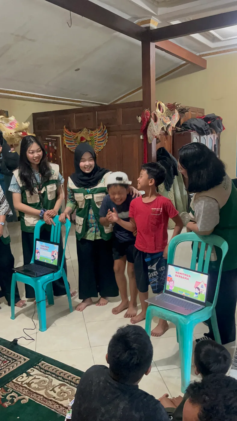 Mahasiswa berdiri bersama anak-anak sambil menunjukkan hasil kegiatan belajar