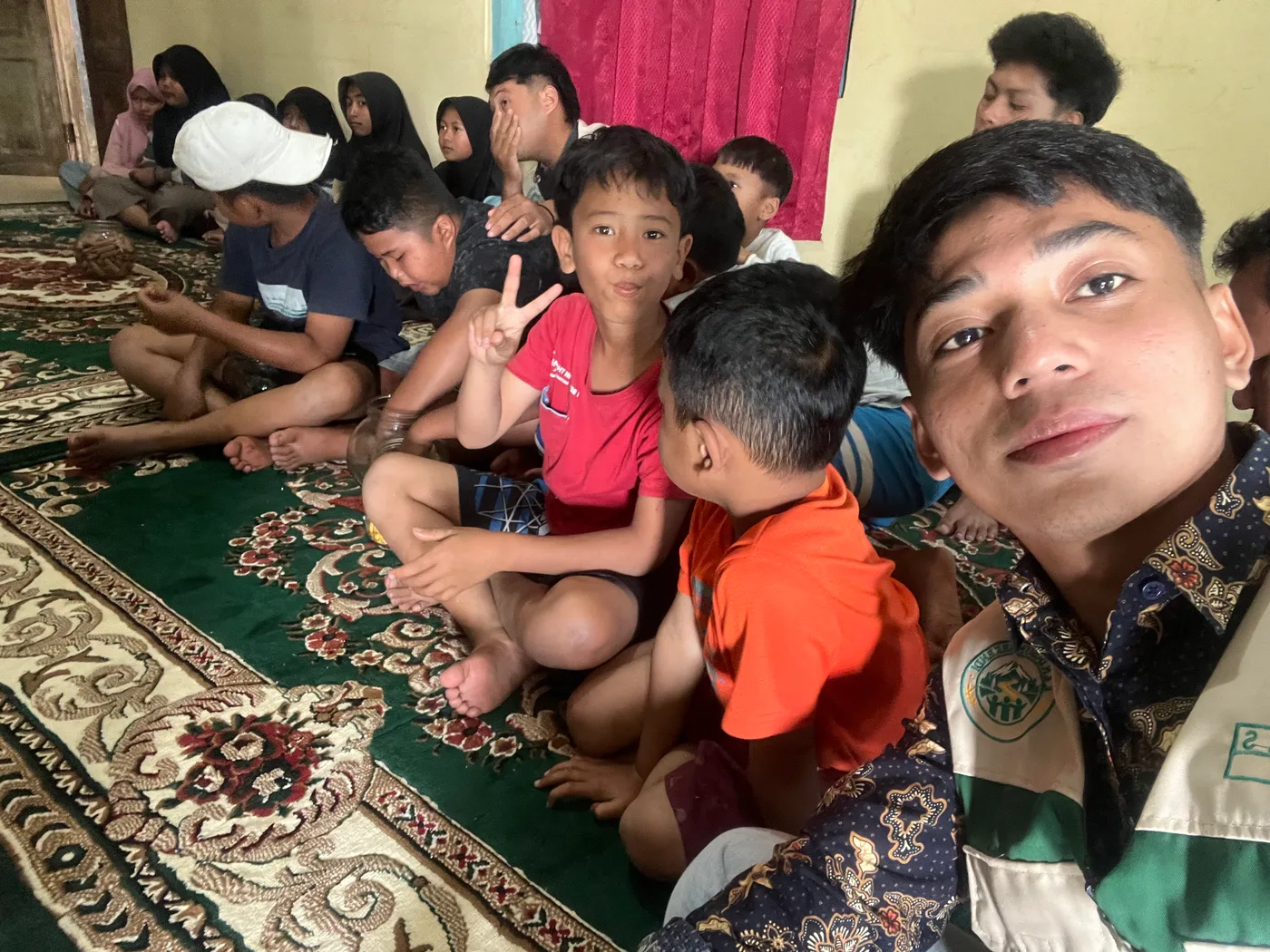 Mahasiswa berselfie dengan anak-anak yang duduk berderet di ruang depan rumah