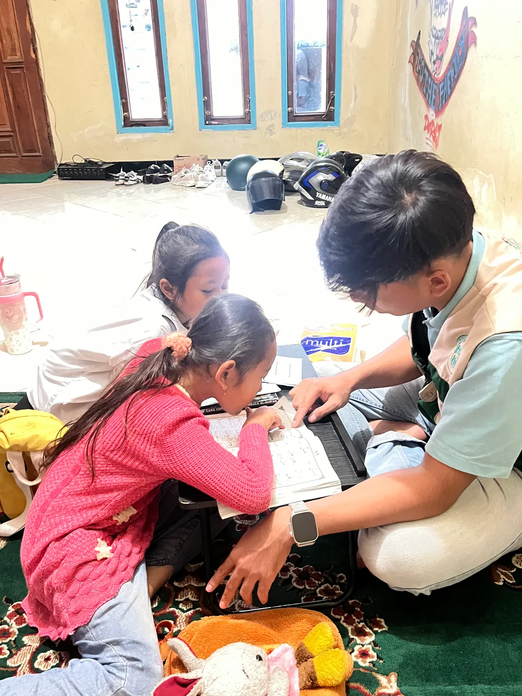 Seorang mahasiswa memeriksa lengan anak perempuan yang duduk di atas karpet