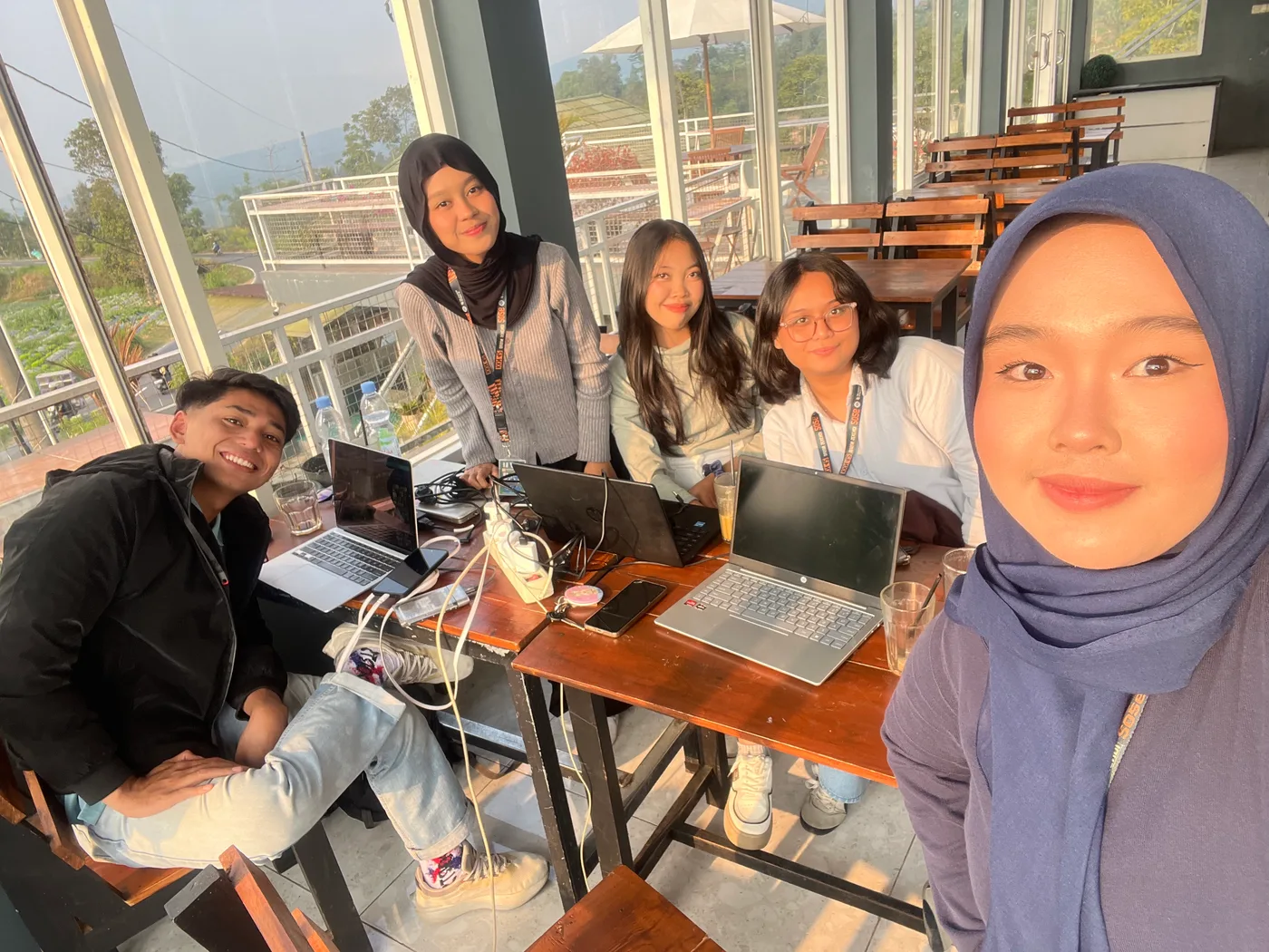 Lima anggota kelompok berselfie bersama di sebuah tempat singgah dengan jendela besar