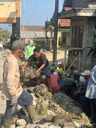 Mahasiswa dan warga mengangkat batu bersama dari saluran drainase di tepi jalan
