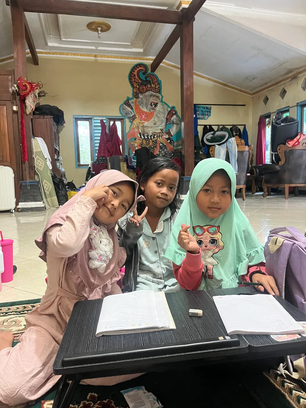 Tiga anak perempuan duduk di depan meja kecil saat kegiatan belajar bersama