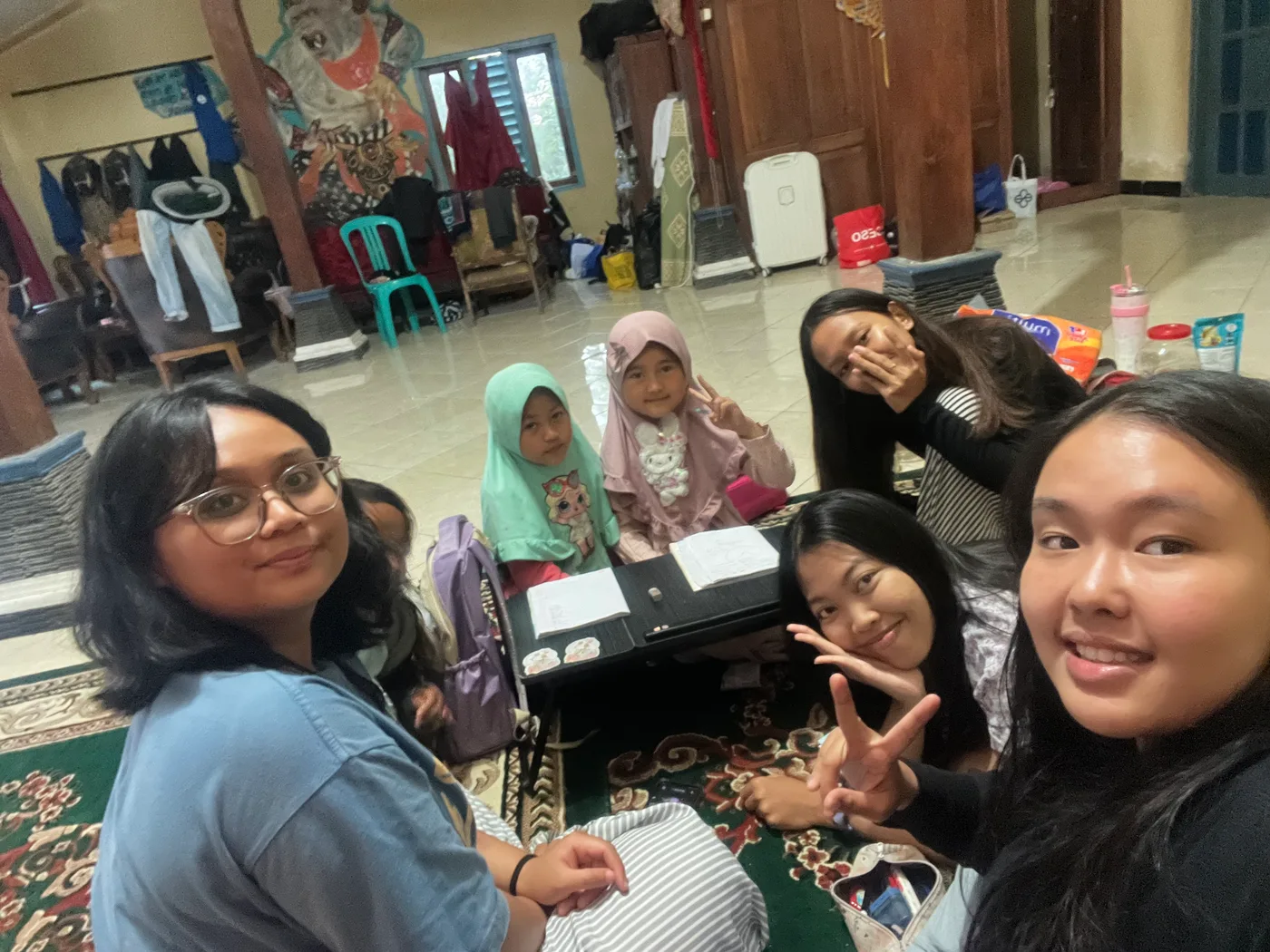 Mahasiswa berselfie dengan anak-anak di sekitar meja belajar dalam ruangan