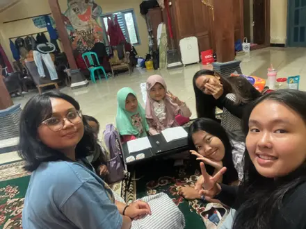 Mahasiswa berselfie dengan anak-anak di sekitar meja belajar dalam ruangan