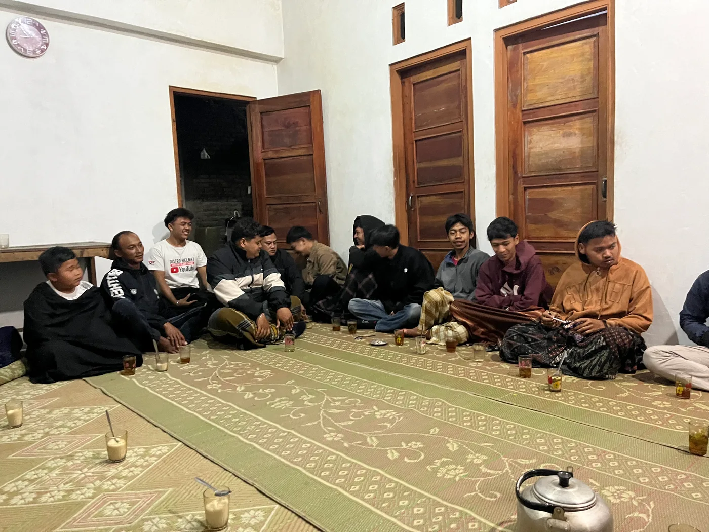 Mahasiswa dan warga duduk berhadapan di balai kecil dalam pertemuan malam