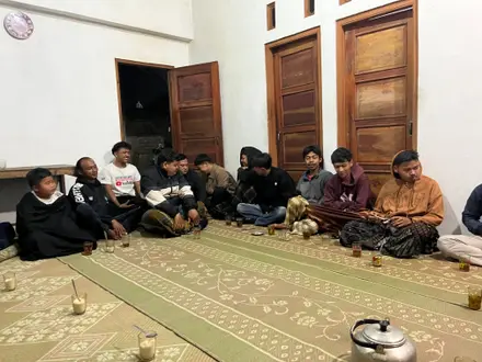 Mahasiswa dan warga duduk berhadapan di balai kecil dalam pertemuan malam