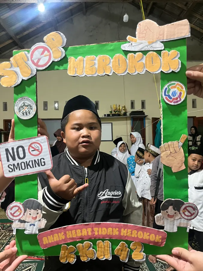 Seorang anak berpeci berpose di dalam bingkai hijau kampanye stop merokok
