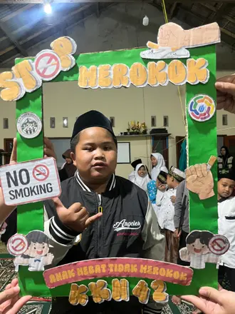 Seorang anak berpeci berpose di dalam bingkai hijau kampanye stop merokok