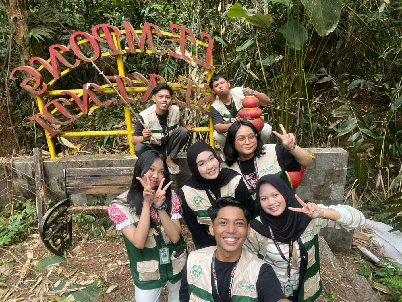 Anggota kelompok berfoto bersama di depan penanda tempat wisata di tengah pepohonan