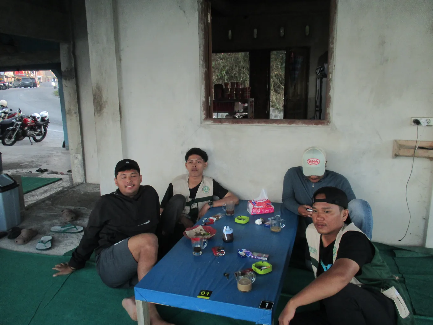 Empat anggota KKN duduk santai mengitari meja kecil di teras rumah