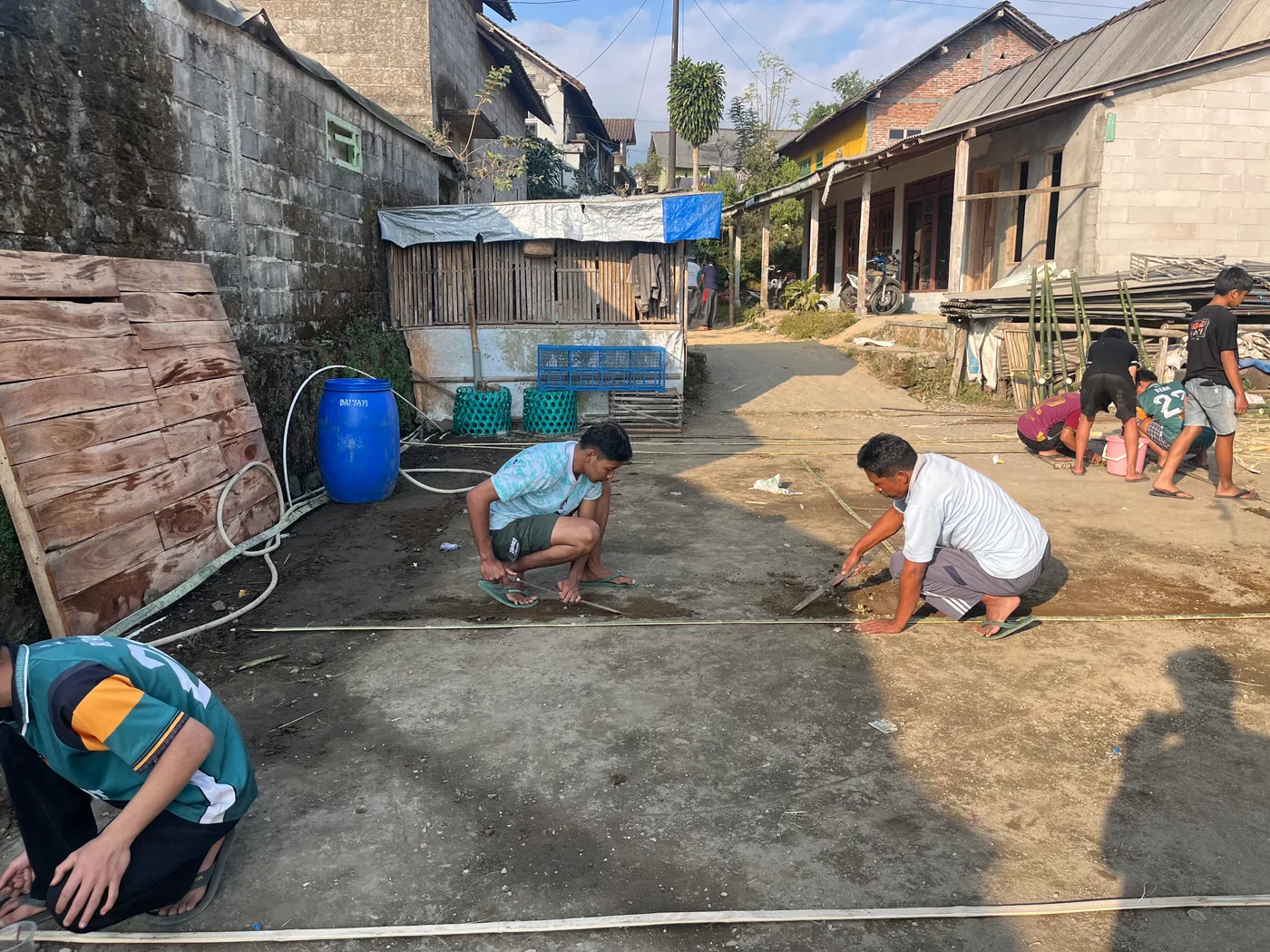 Anak-anak jongkok menggambar dan bermain bersama mahasiswa di halaman beton