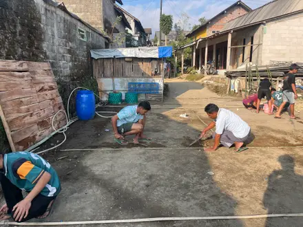 Anak-anak jongkok menggambar dan bermain bersama mahasiswa di halaman beton
