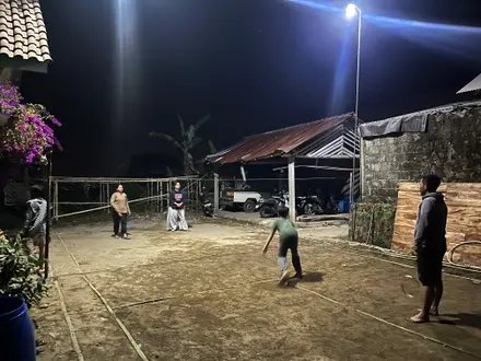 Warga dan mahasiswa bermain bulu tangkis di lapangan dusun pada malam hari